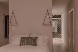 Quarto com cama, duas prateleiras suspensas e vista para um corredor com parede azulejada.