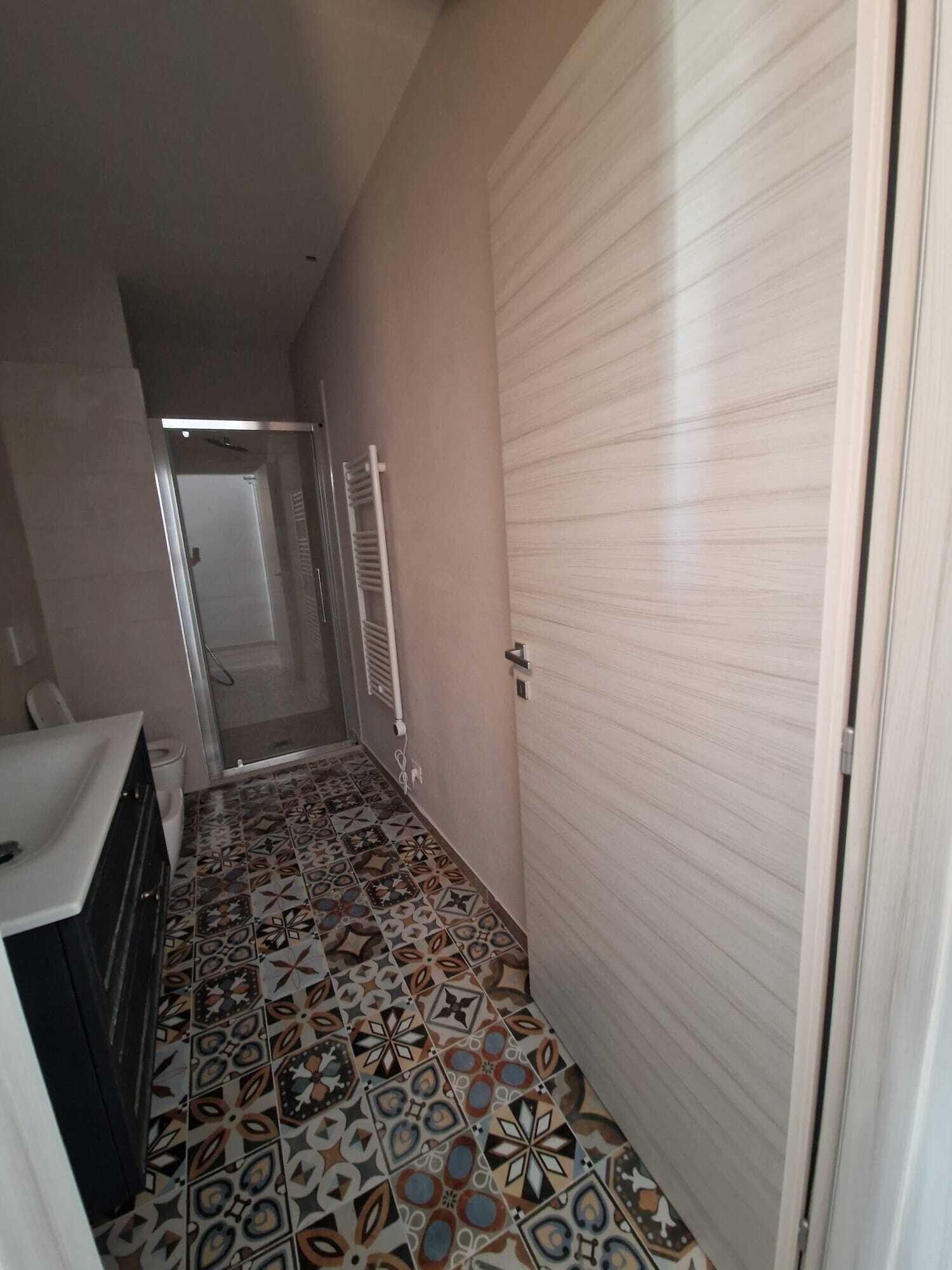 Un pasillo estrecho con baldosas estampadas, una puerta blanca y un radiador blanco.