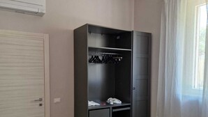 Une chambre avec une armoire, deux lits, une lampe suspendue rouge et une fenêtre ornée de rideaux légers.