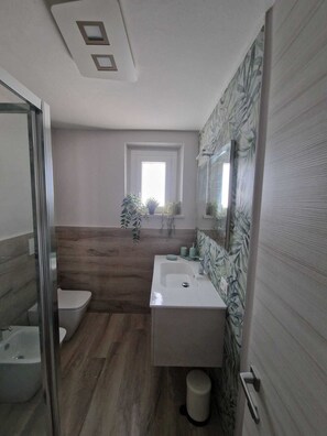 Een moderne badkamer met een houten vloer, een wit wastafelmeubel en een grote spiegel.