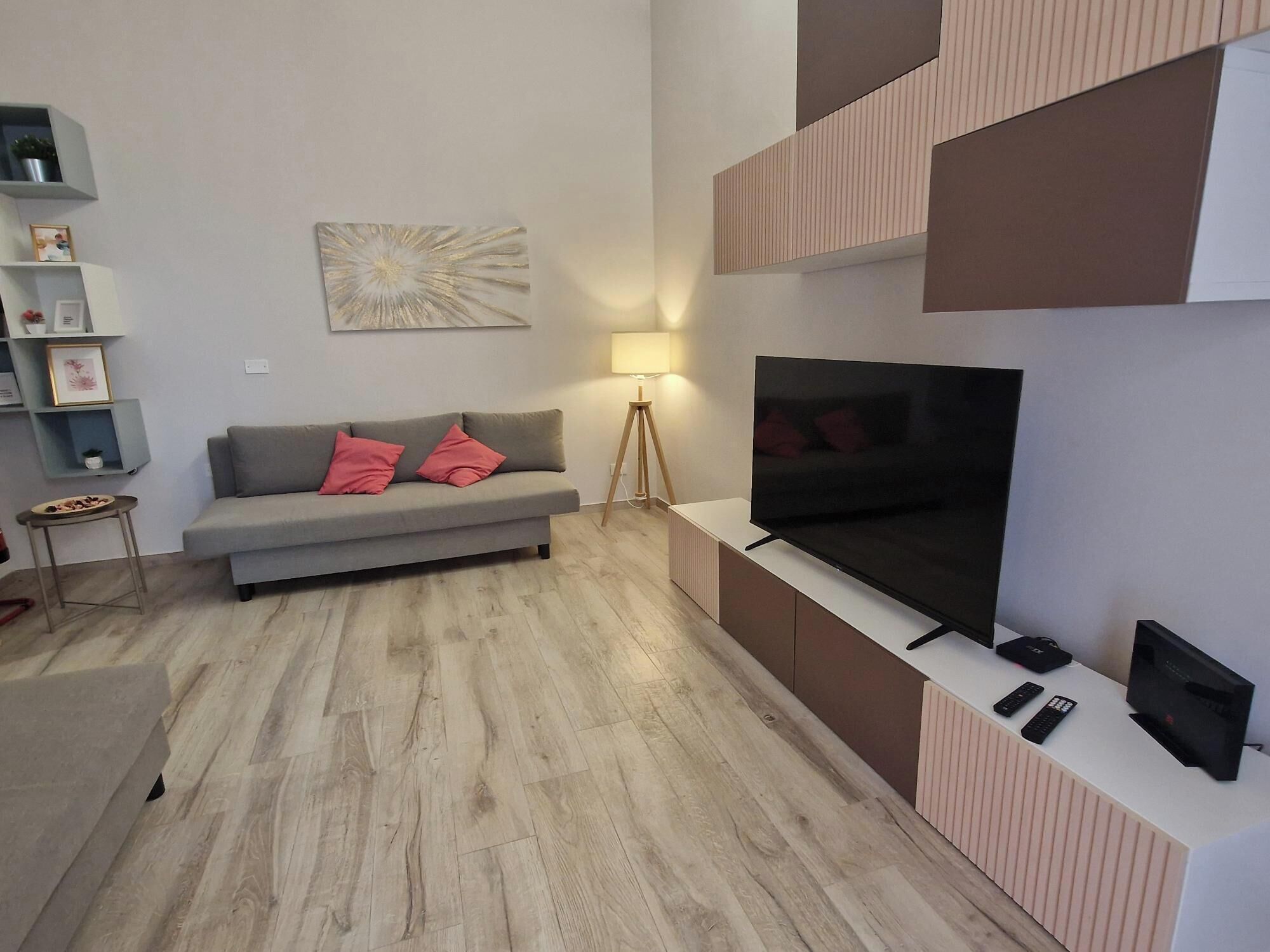 A modern living room with a grey sofa, red cushions, a flat-screen TV, and a minimalist decor.