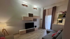 Un salon moderne avec un téléviseur à écran plat, un canapé, une lampe et une plante.