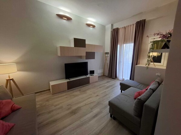 A modern living room with a flat-screen TV, a sofa, a lamp, and a plant.