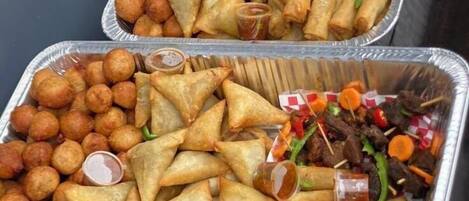 Two trays of samosas and other snacks, each accompanied by a small container of sauce.
