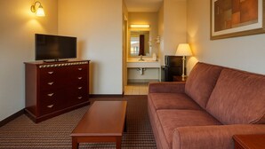 Quarto de hotel com sofá, televisão em uma cômoda, luminária, quadro e banheiro visível por uma porta aberta.