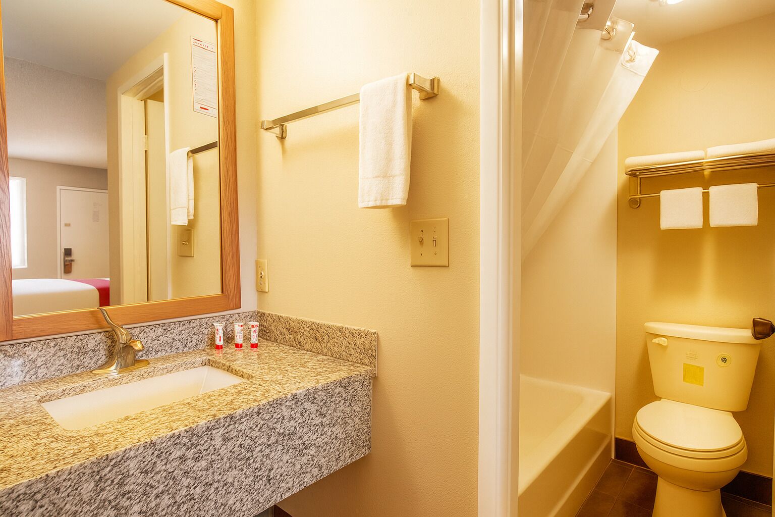 A bathroom with a granite countertop, a mirror, a towel rack, a toilet, and a shower curtain.