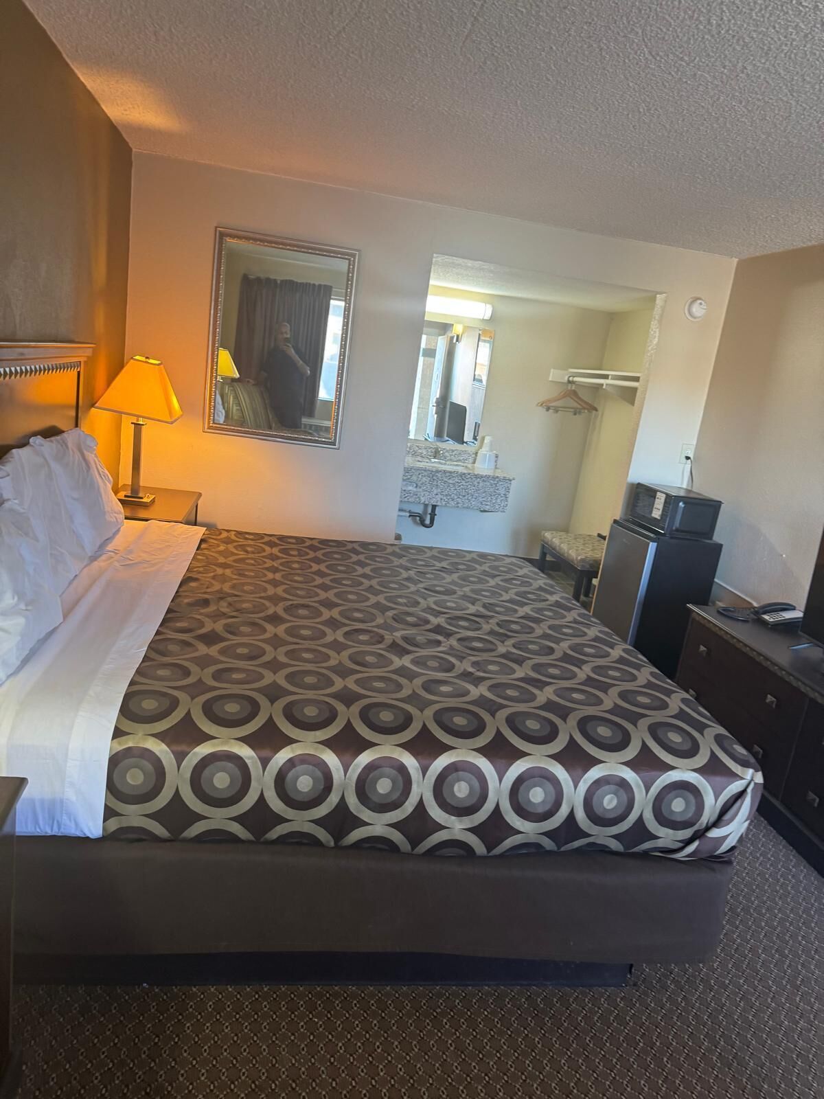 Ein Hotelzimmer mit Bett, Nachttisch, Lampe, Kommode und Spiegel.