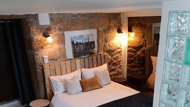A bedroom with a stone wall, a wooden headboard, a bed with white and brown bedding, a small round table, and a glass partition.