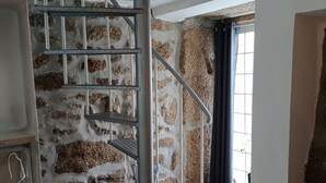 A spiral staircase with metal railings, a stone wall, and a window with curtains.