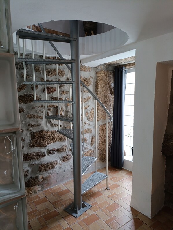 Una escalera de caracol con barandillas de metal, un muro de piedra y una ventana con cortinas.