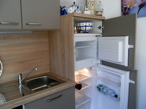 A kitchen with a built-in sink, a white refrigerator, and a wooden cabinet above the sink.