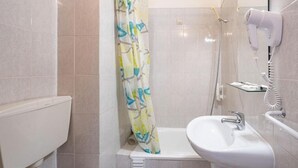 Een badkamer met een douche, toilet, wastafel en een aan de muur bevestigde haardroger.