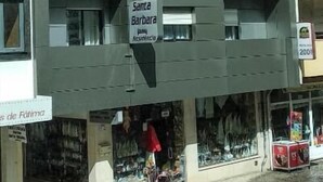 Een meerhoog gebouw met een grijze gevel, een bord met 'Santa Barbara' en een winkel beneden met diverse spullen in etalage.