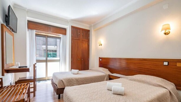 Een hotelkamer met twee bedden, een bureau, een stoel en een televisie.