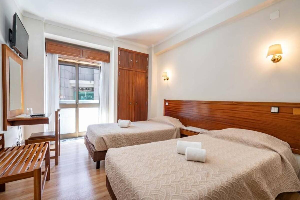 Quarto de hotel com duas camas, uma mesa, uma cadeira e uma televisão.