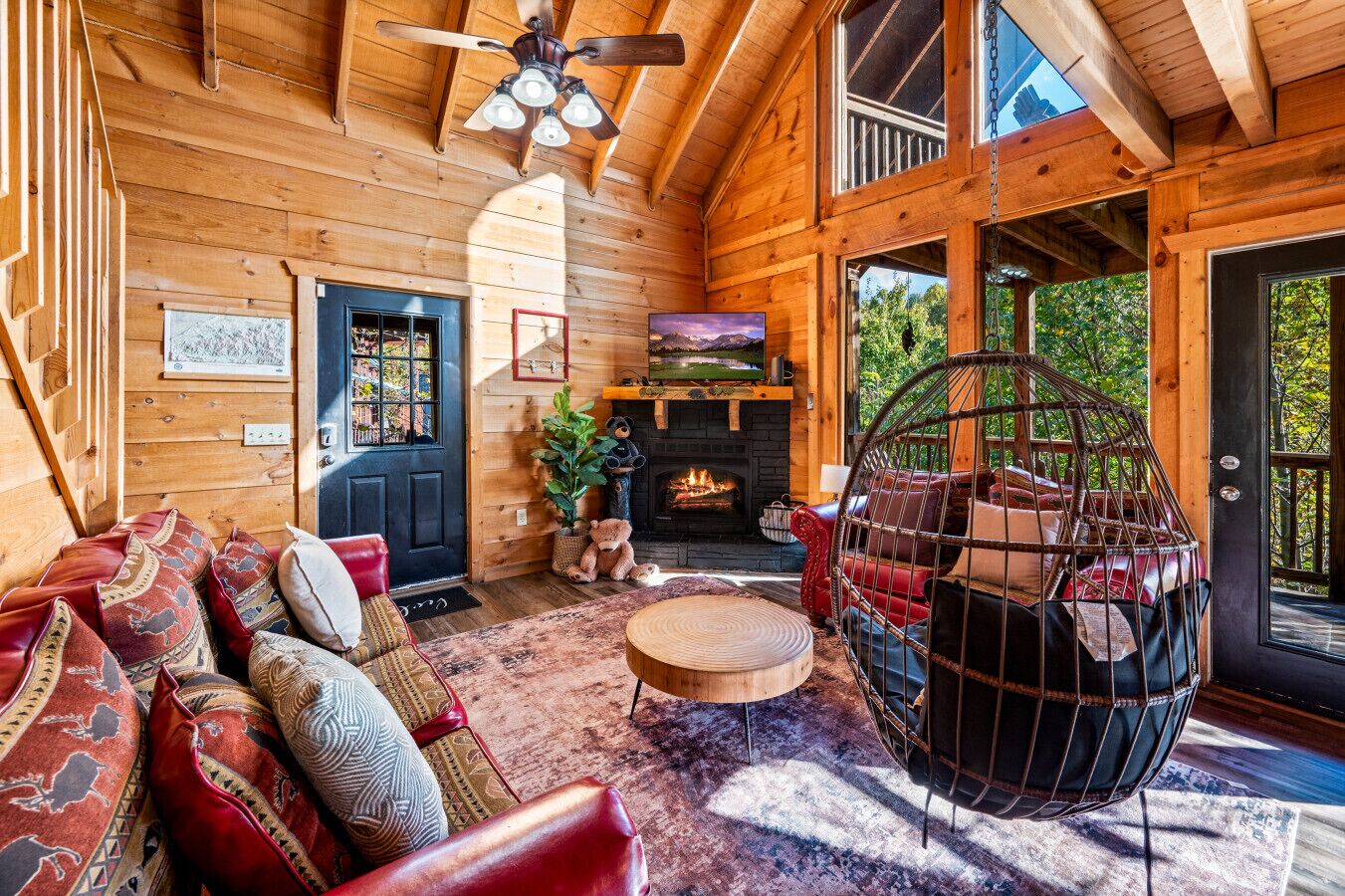 A cozy log cabin interior with a fireplace, a hanging chair, and a sofa with patterned cushions.