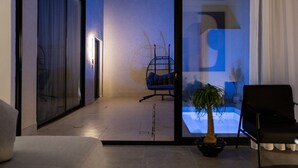 A modern living room with a glass door leading to a balcony, a hanging chair, a potted plant, and a black chair. - Nolina chalets (Madinah)