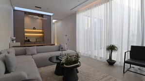 A modern living room with a grey sofa, a round coffee table with a plant, a black armchair, and a large window with sheer curtains. - Nolina chalets (Madinah)