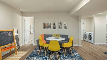 A modern living room with a round table, yellow chairs, a gray sofa, and a blue patterned rug.