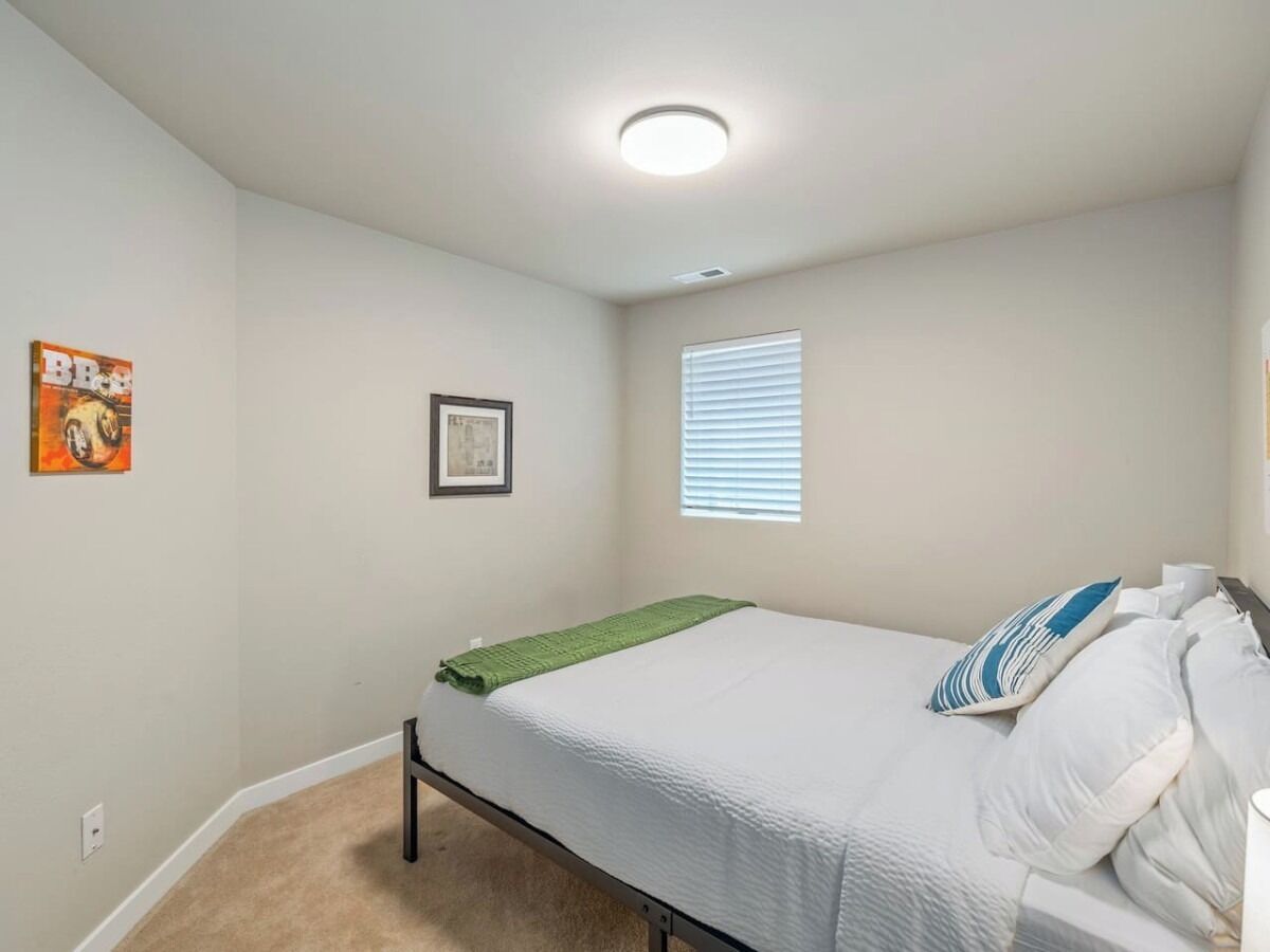 A bedroom with a bed, a window with blinds, a framed picture on the wall, and a carpeted floor.