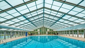 En inomhuspool med ett glastak, omgiven av solstolar och med fri utsikt över omgivningen.