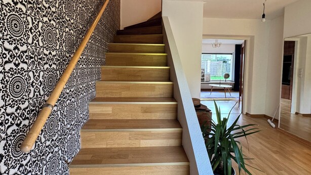 A staircase with a patterned carpet, wooden steps, and a handrail. There is a potted plant on the landing. - Central and quiet living in Bonn (Bonn)