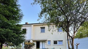A two-story residential building with a white facade, a visible number '16', and a small front garden with a hedge and a tree. - Central and quiet living in Bonn (Bonn)
