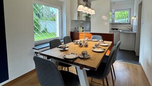 A modern kitchen with white cabinets, a dining table set with plates and cups, and a view of the outdoors through large windows. - Central and quiet living in Bonn (Bonn)