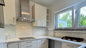 A modern kitchen with white cabinets, a stainless steel range hood, a window with a view, and a built-in dishwasher. - Central and quiet living in Bonn (Bonn)