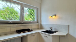 A modern kitchen with white cabinetry, a black countertop, a window with a view of greenery, and a wall-mounted light fixture. - Central and quiet living in Bonn (Bonn)