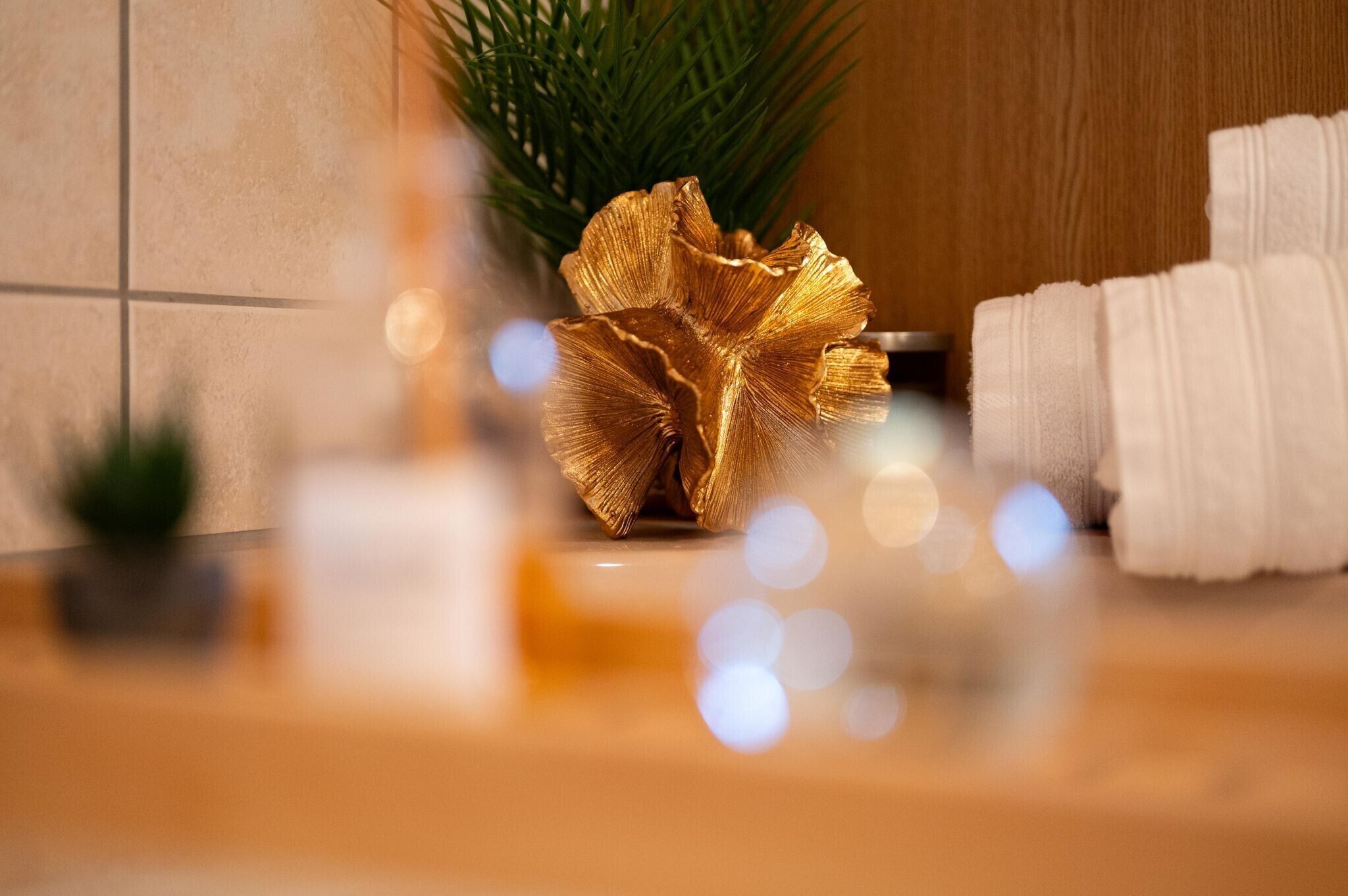 A bathroom with a golden decorative piece, white towels, and a small plant.