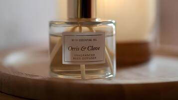 Een vierkante fles 'Orris & Clove' rietverspreider met een etiket, geplaatst op een ronde tafel met een onscherpe achtergrond.