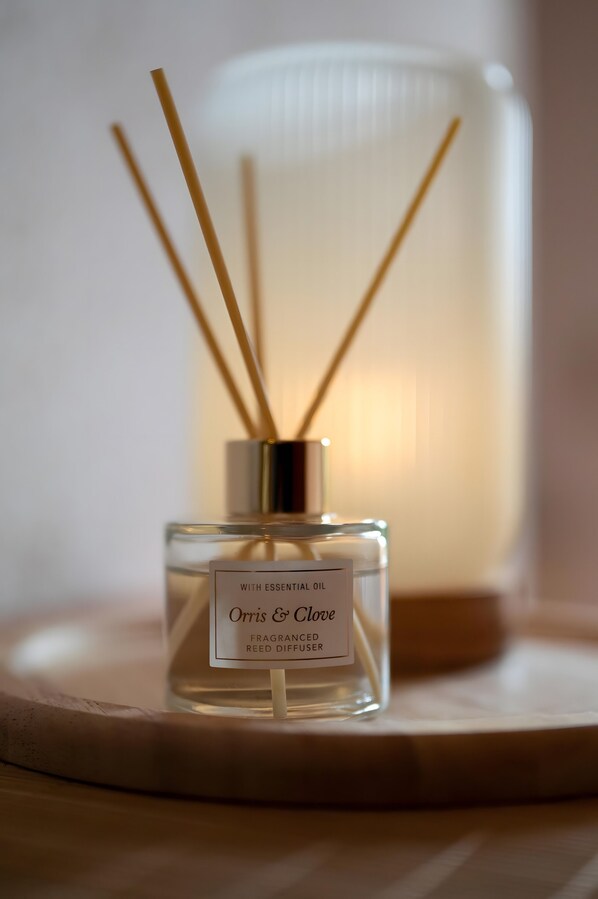 Un flacon carré contenant un diffuseur de parfum aux senteurs d’iris et de girofle, orné d’une étiquette, est posé sur une table ronde, avec un arrière-plan flou.