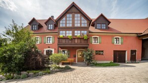 Ein großes, zweistöckiges Gebäude mit roter Fassade, zahlreichen Fenstern und einem zentralen Balkon mit Pflanzen.