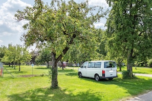 Un fourgon blanc est garé dans une zone herbeuse, avec des arbres et une clôture en arrière-plan.