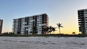 A beachfront hotel with multiple floors, balconies, and a sandy beach in the foreground.