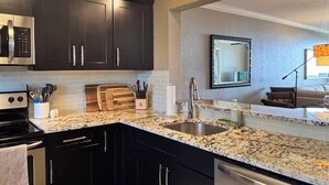 A modern kitchen with dark cabinets, granite countertops, a stainless steel sink, and a built-in microwave.