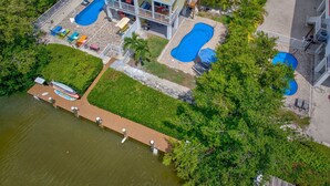 Uma casa de dois andares com um deck espaçoso, duas piscinas e um cais com barcos.