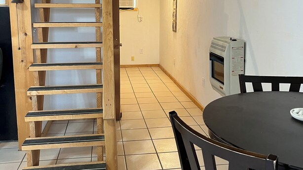 A wooden staircase leading to a loft bedroom, a dining table with chairs, and a wall-mounted oven.