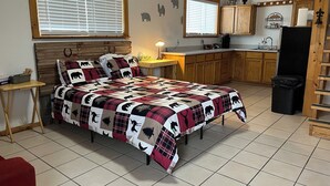 A bedroom with a bed, a wooden headboard, a nightstand, a desk, and a window with blinds.