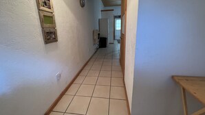 A narrow hallway with tiled flooring, a wooden bench, and a wall-mounted clock.