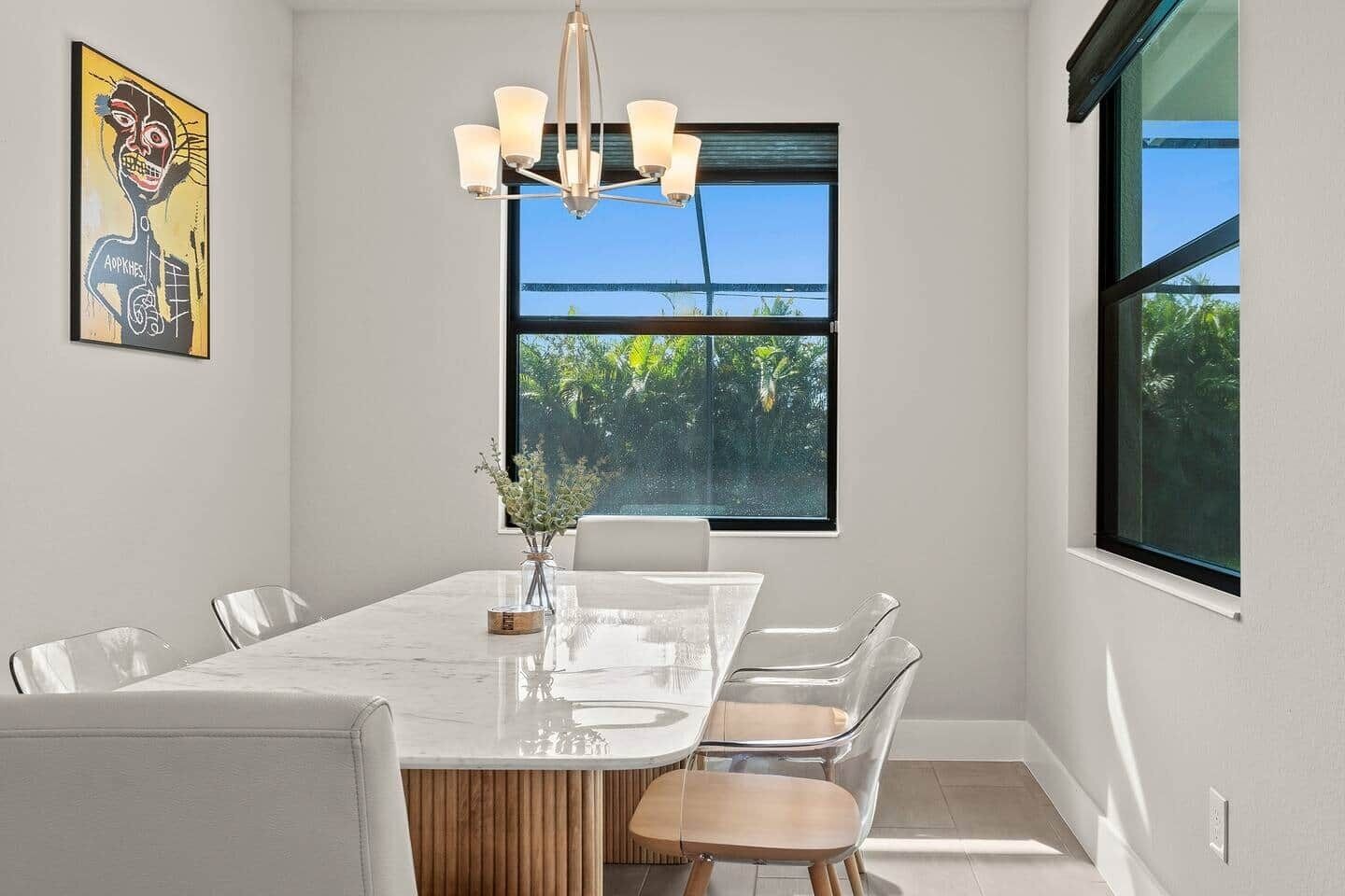 Un espace repas comprenant une table en marbre, des chaises transparentes, un élément décoratif en bois et un lustre.