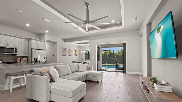A modern living room with a sectional sofa, a kitchen area, and a large TV. - Biohackers Retreat - Heated Pool, Spa, Sauna, Gym (Cape Coral)