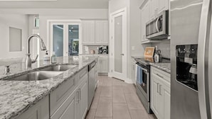 A modern kitchen with granite countertops, stainless steel appliances, and white cabinetry. - Biohackers Retreat - Heated Pool, Spa, Sauna, Gym (Cape Coral)