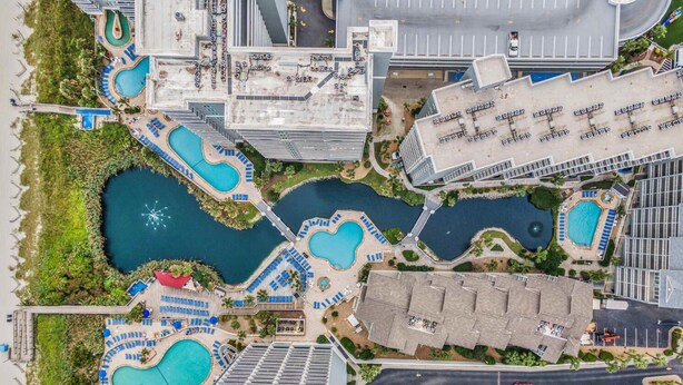 Vista aérea de un resort con varias piscinas, un estacionamiento y edificios circundantes.