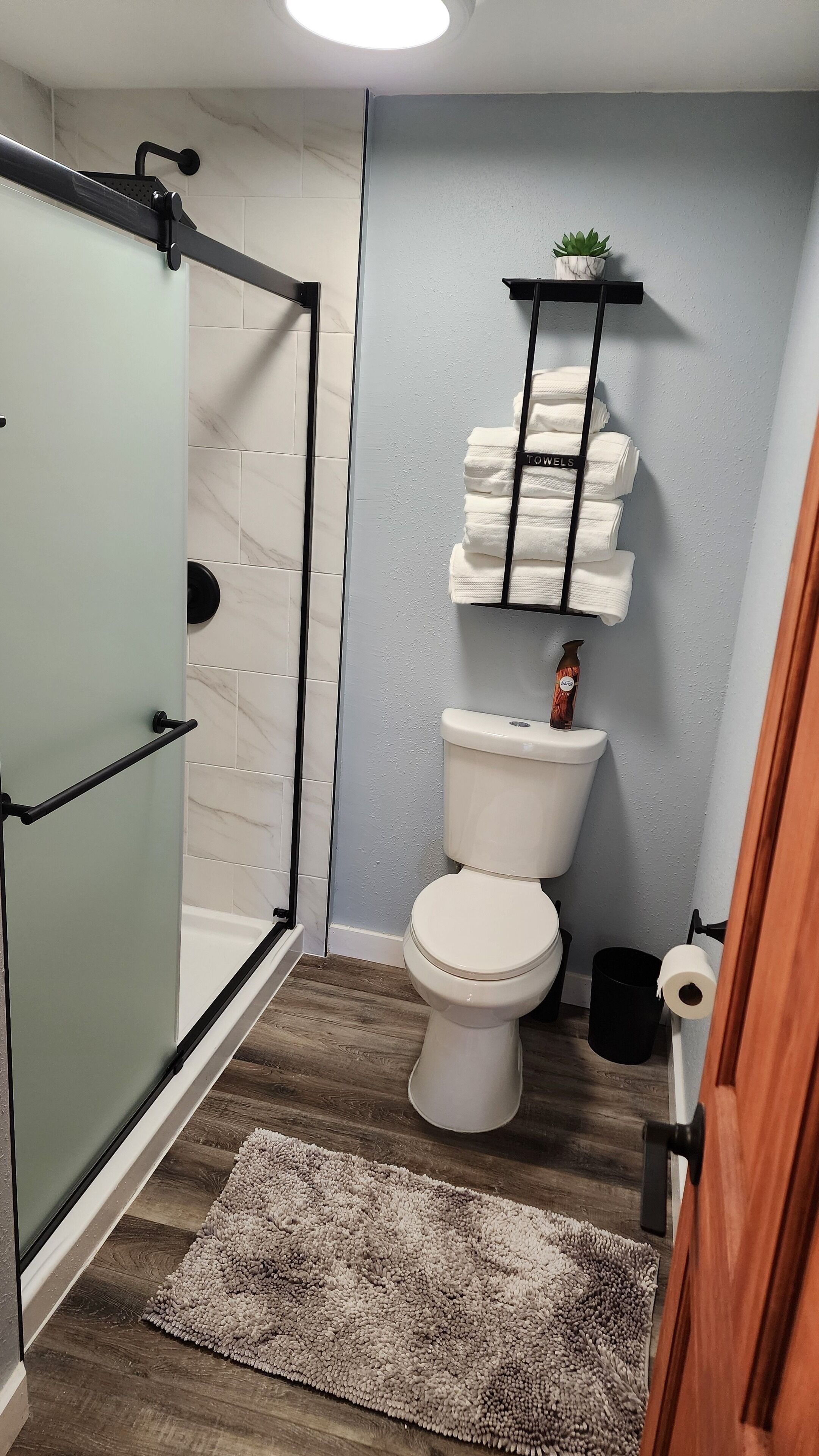 Et badeværelse med en brusekabine i glas, toilet med håndklæderadiator og trægulv.