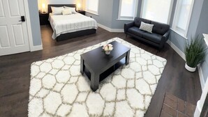 Ein modernes Schlafzimmer mit einem Bett, Nachttischen und einem Beistelltisch. Es gibt eine Sitzecke mit einer Couch und einem Couchtisch. Der Raum verfügt über große Fenster und eine Deckenleuchte.