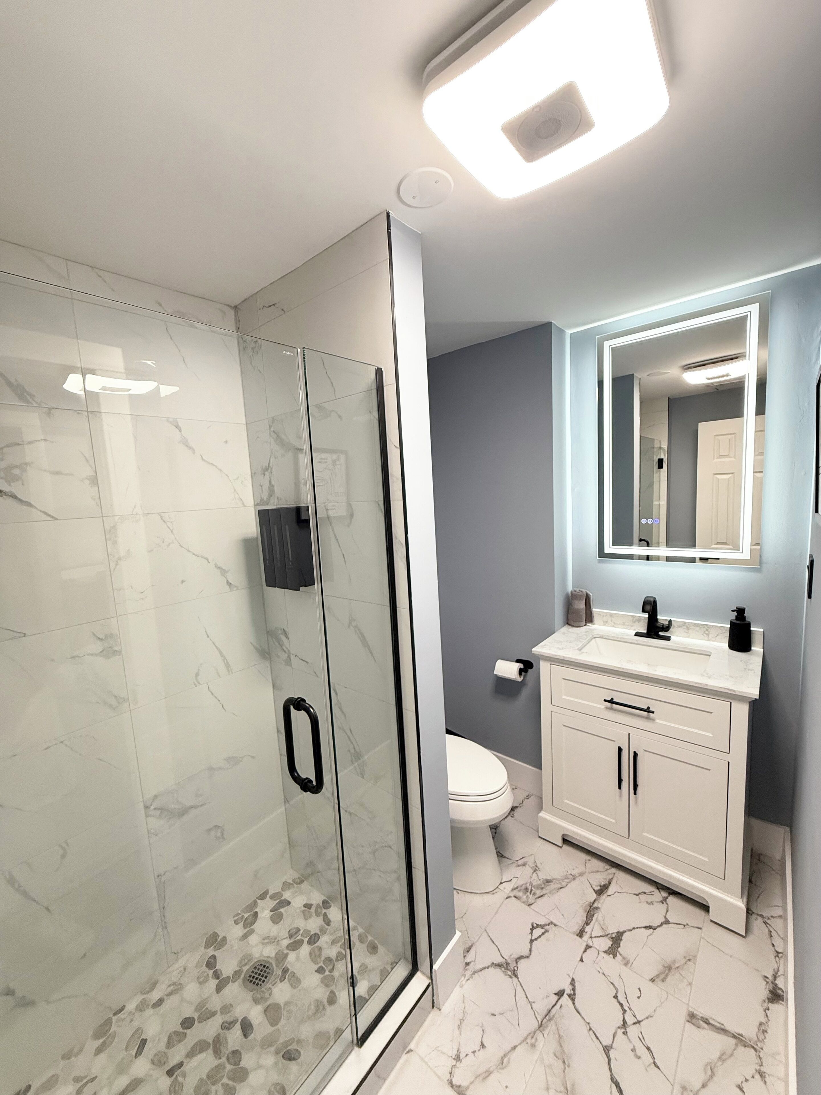 A modern bathroom with a glass-enclosed shower, a white vanity with a mirror, and marble flooring.