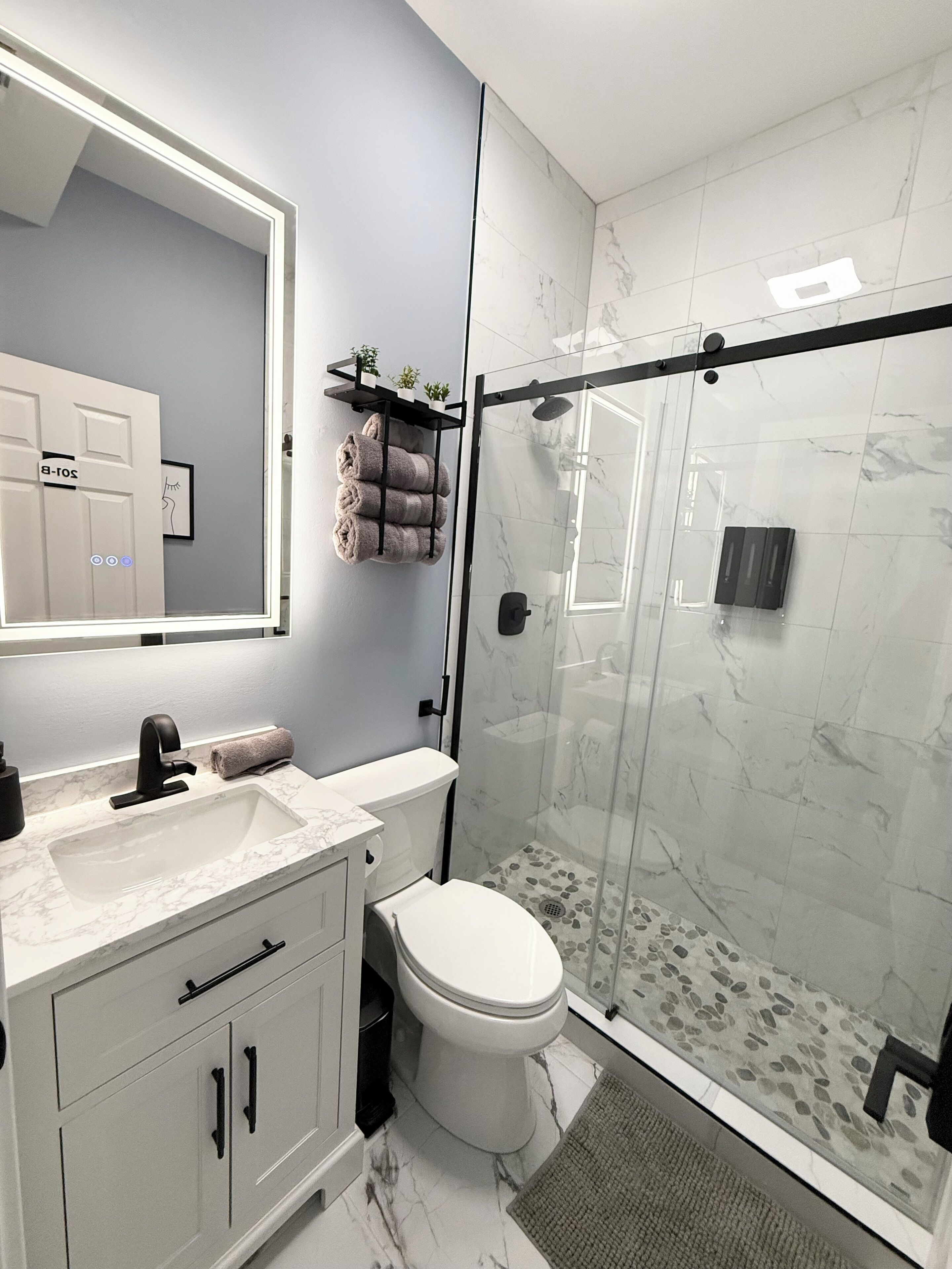 A modern bathroom with a glass-enclosed shower, a white toilet, and a marble sink.