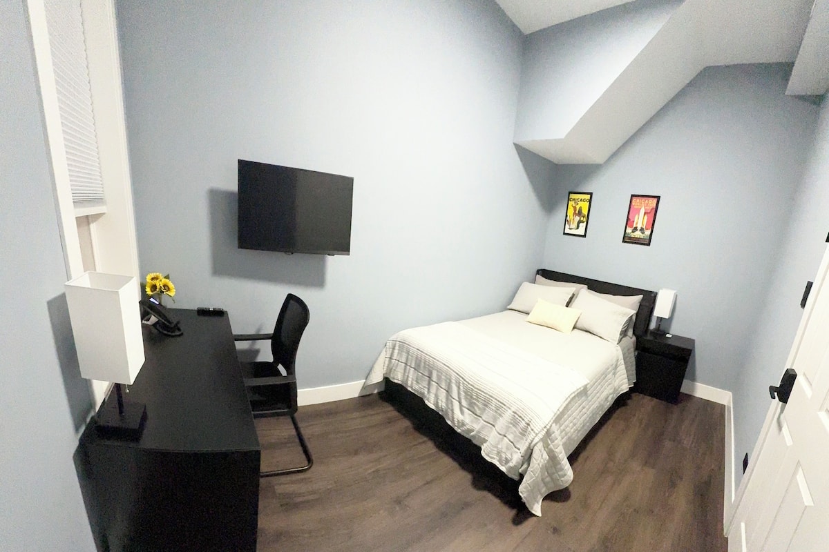 Ein Schlafzimmer mit einem Bett, einem Schreibtisch, einem Stuhl, einem Fernseher und zwei gerahmten Bildern an der Wand.